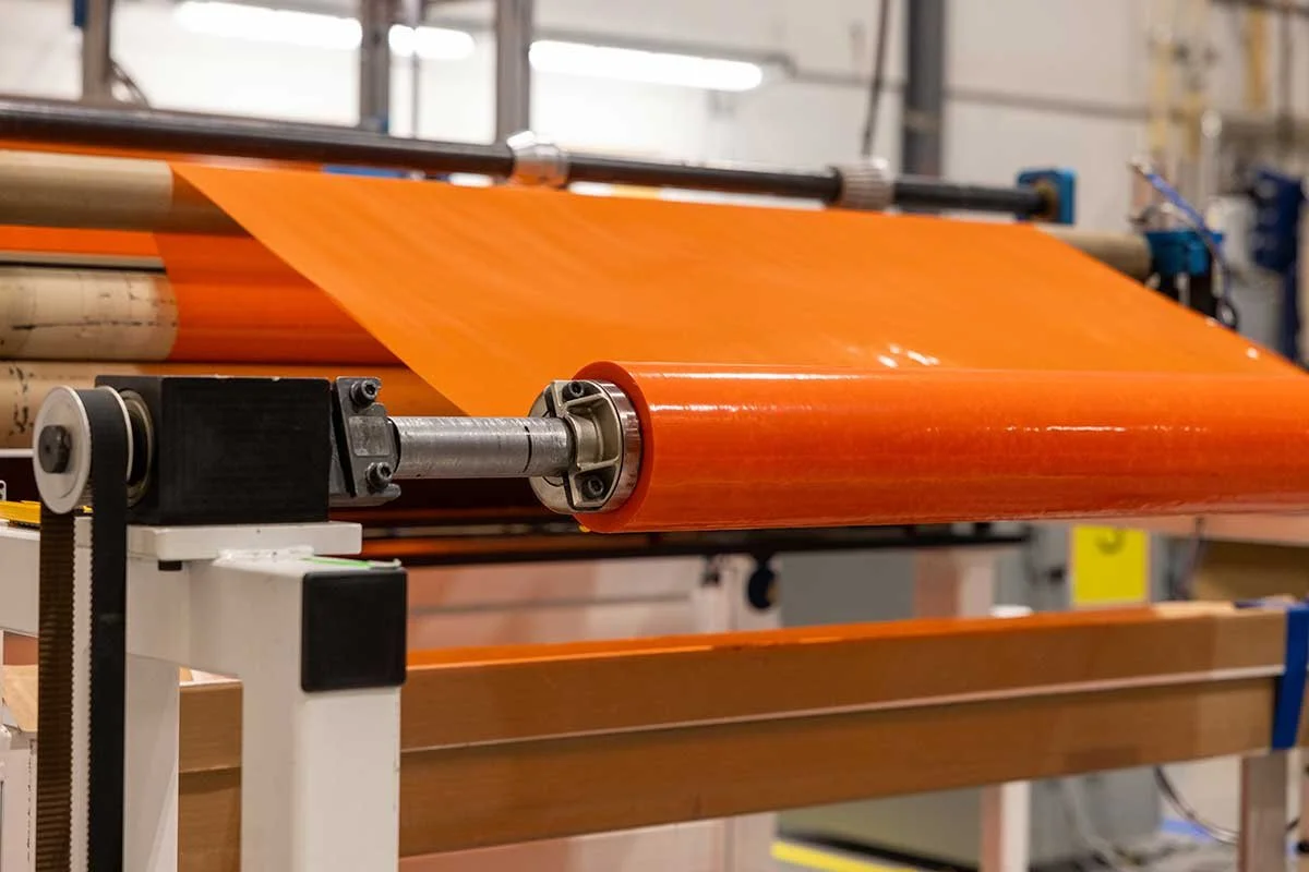 Close-up of an orange-colored material being processed on industrial rollers in a factory setting.