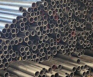 Stacks of 4130 round tubing are piled together, showcasing various lengths and diameters. The metal tubes have a polished, metallic surface and are arranged horizontally, filling the frame.